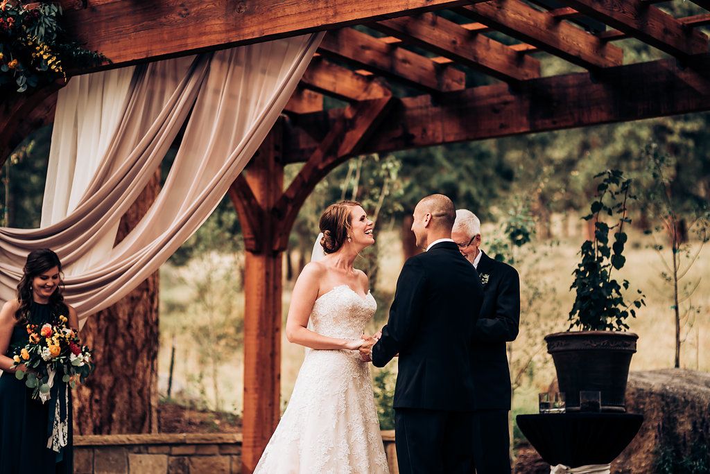 Intimate outdoor wedding ceremony moment under rustic wooden pergola with elegant draping.