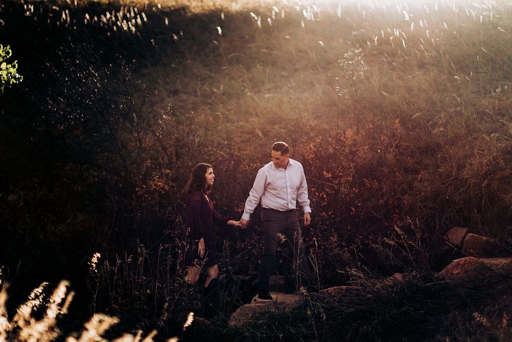 Couple sharing tender moment in sunlit meadow with mountains in background.