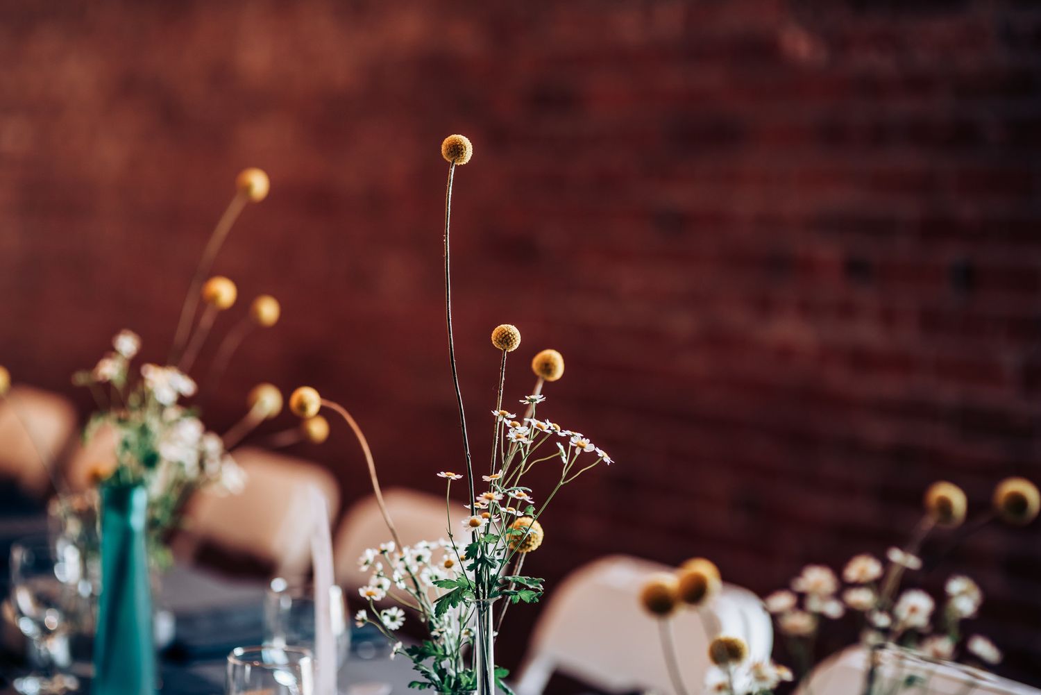 Artistic table centerpiece with yellow billy balls and delicate flowers against red brick.