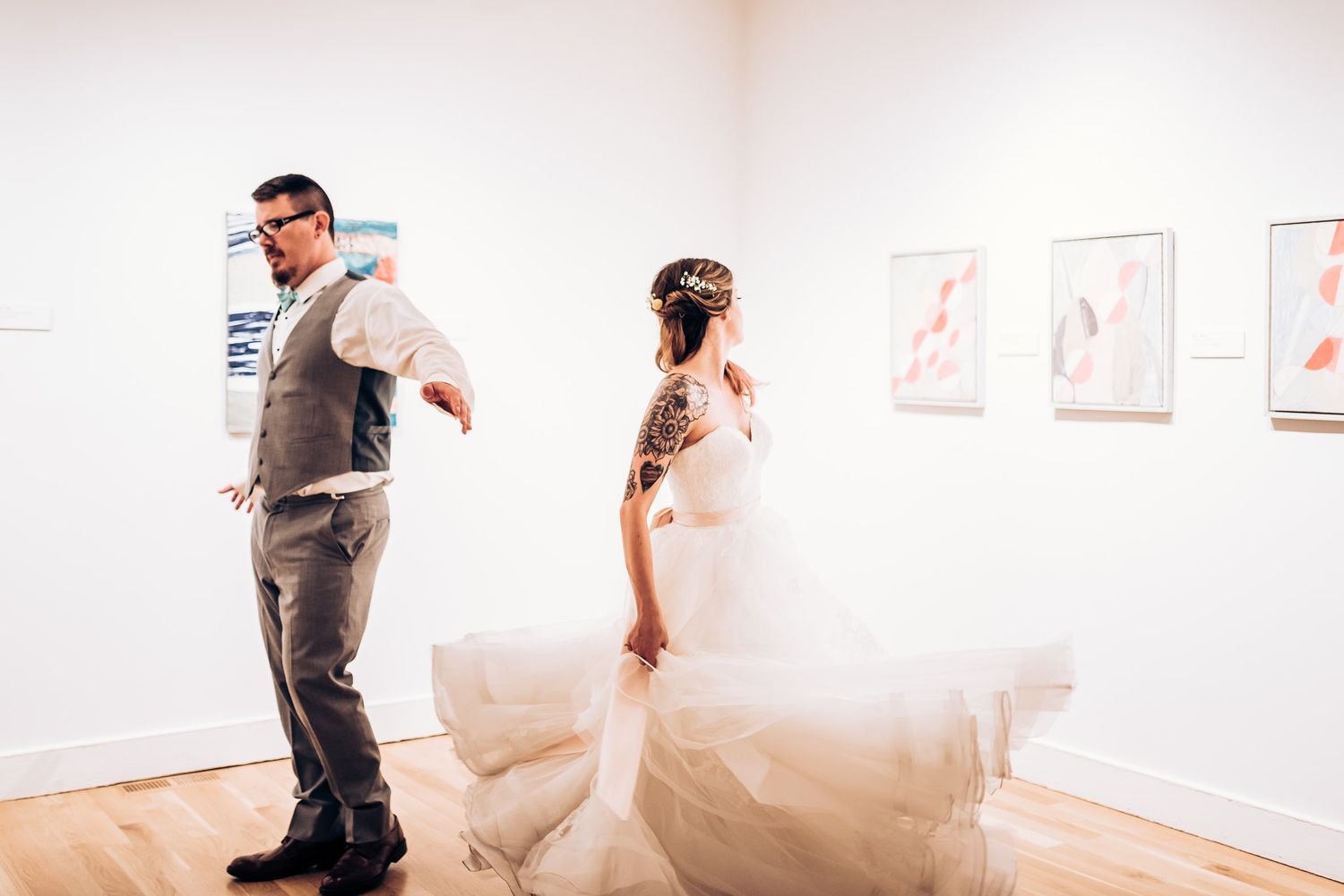 A couple spins and dances in a bright white art gallery with artwork on walls.