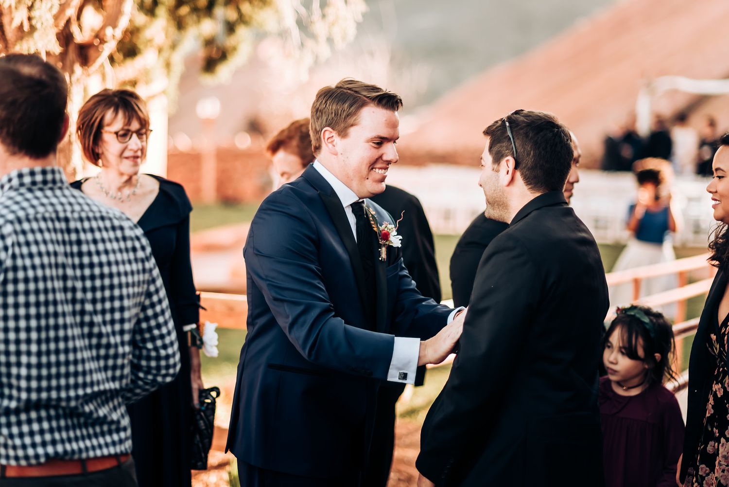 Wedding guests mingling and congratulating each other at outdoor celebration with string lights.