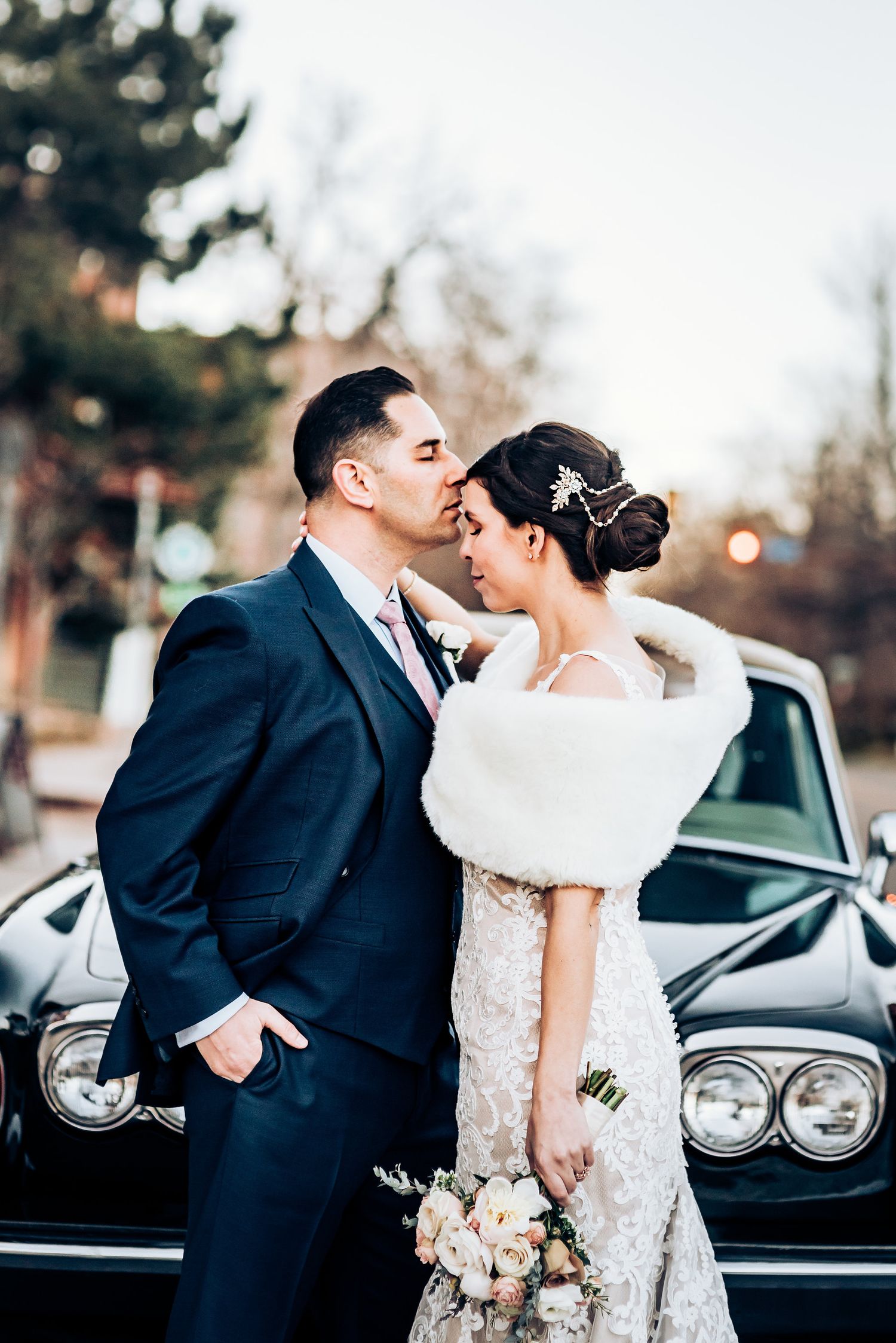 Romantic moment between newlyweds by vintage black car in winter setting.