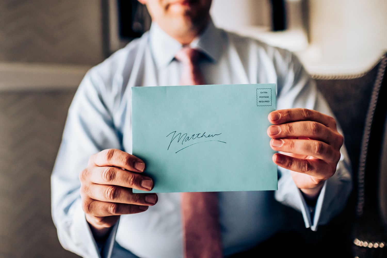 Hands holding a mint green envelope in formal business attire.