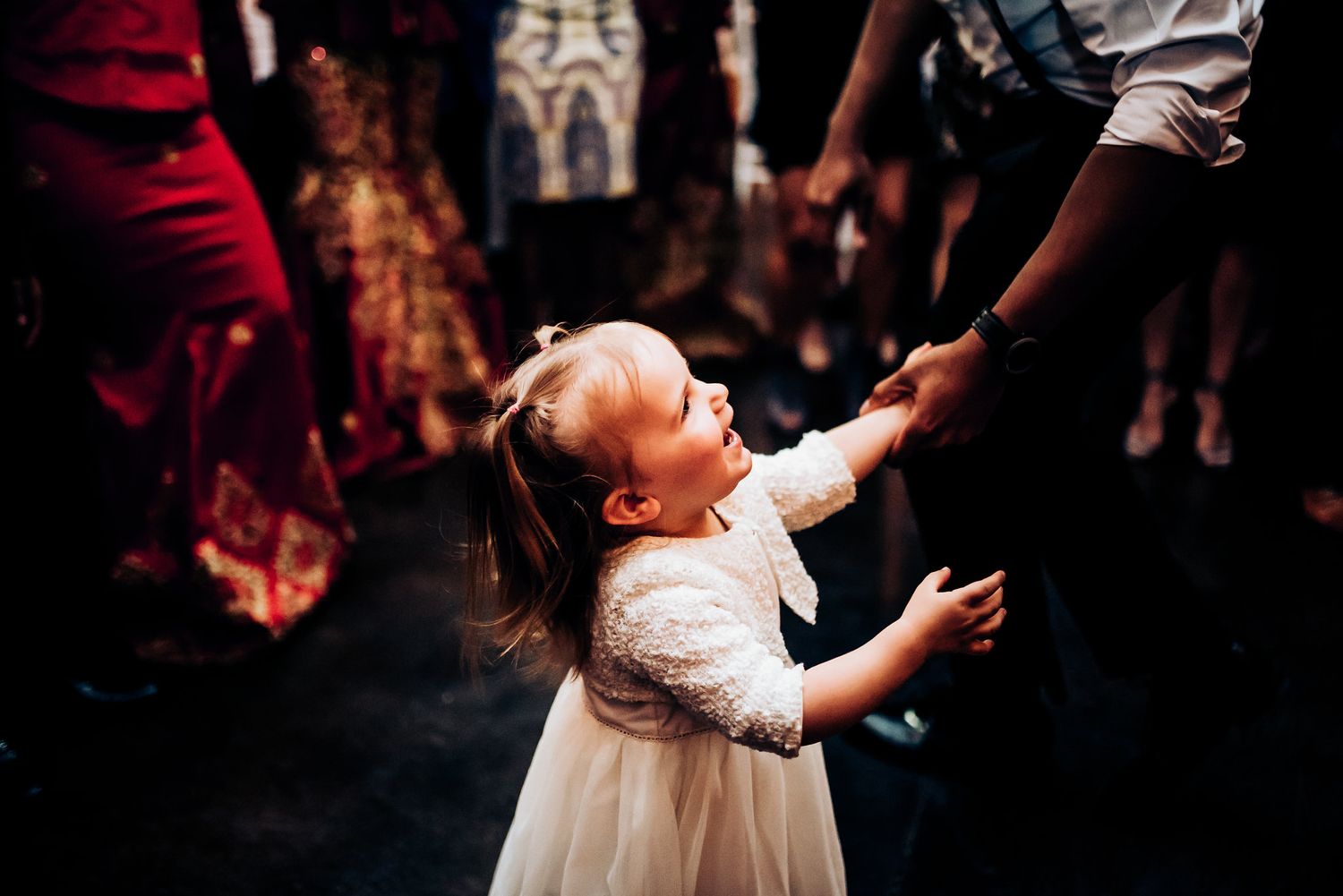 Young flower girl in white dress dances joyfully on reception dance floor.