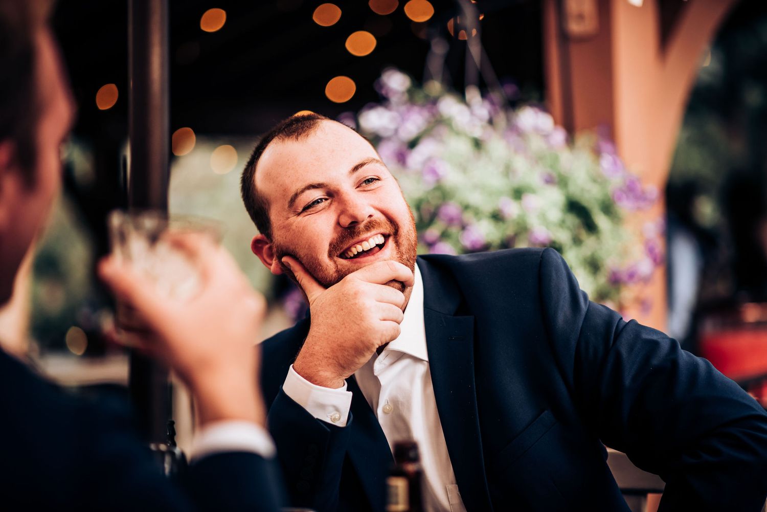 Wedding guest enjoying a lighthearted moment during the reception with bokeh lights in background.
