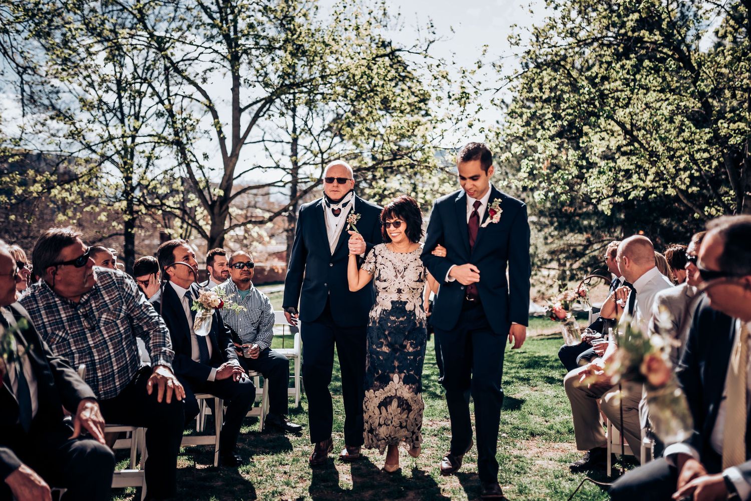 Outdoor spring wedding ceremony with blooming trees and seated guests watching proceedings.