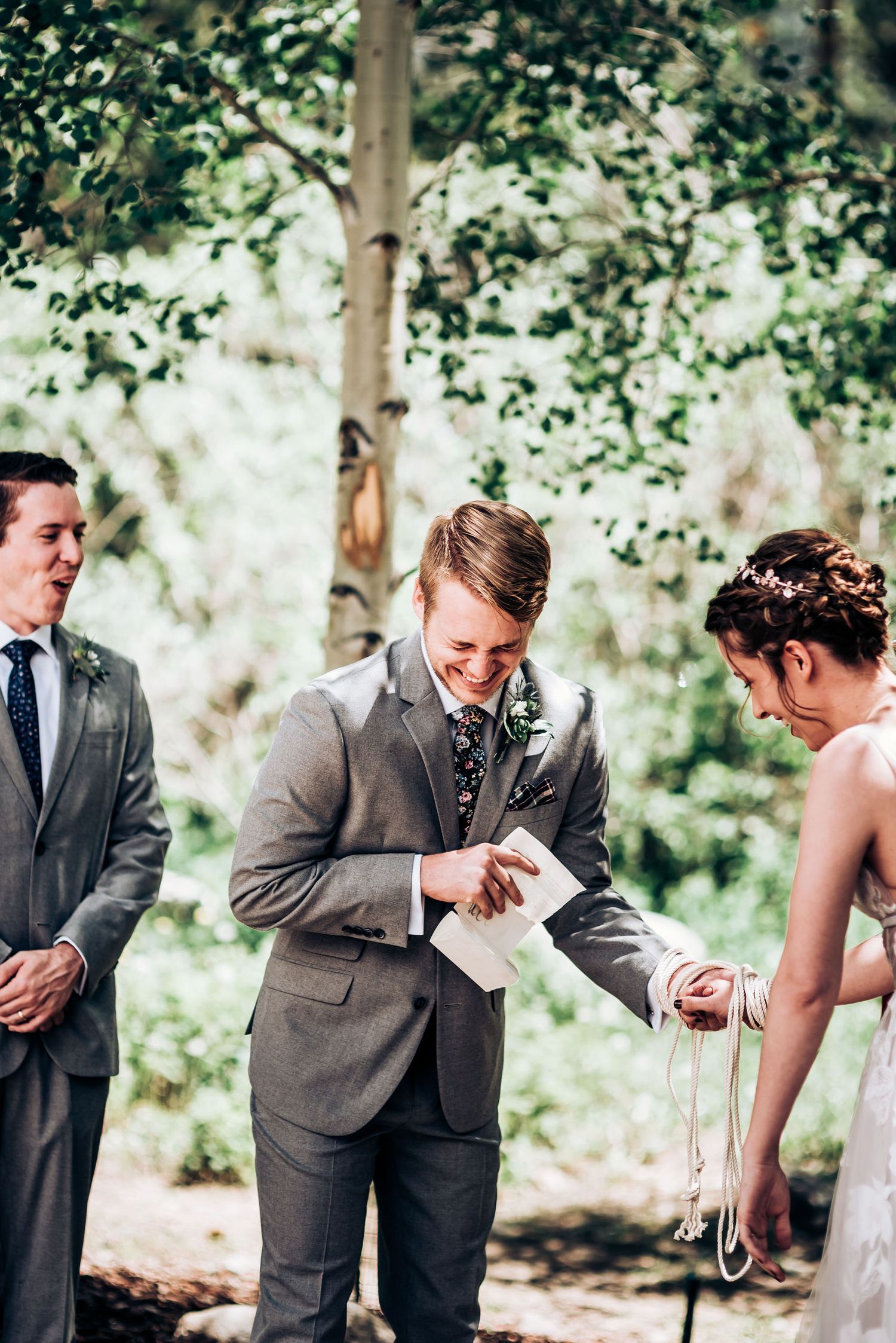 An intimate forest wedding ceremony with couple exchanging rings under tree canopy.