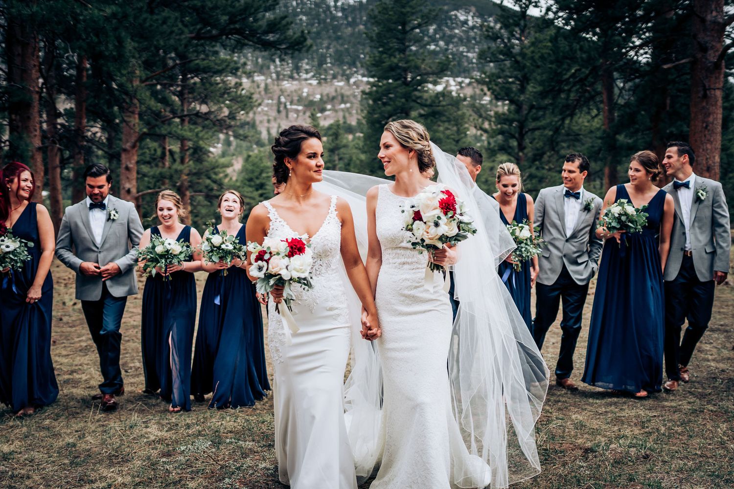 Wedding party in navy blue and gray attire poses together in a forest setting.