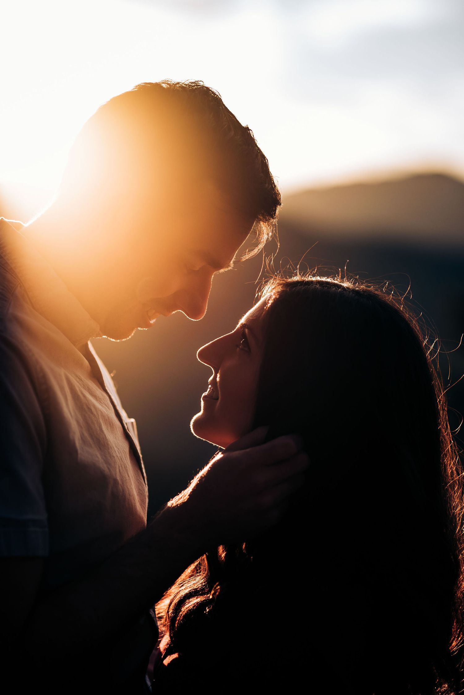 Silhouetted couple shares intimate moment in warm backlit sunset glow.