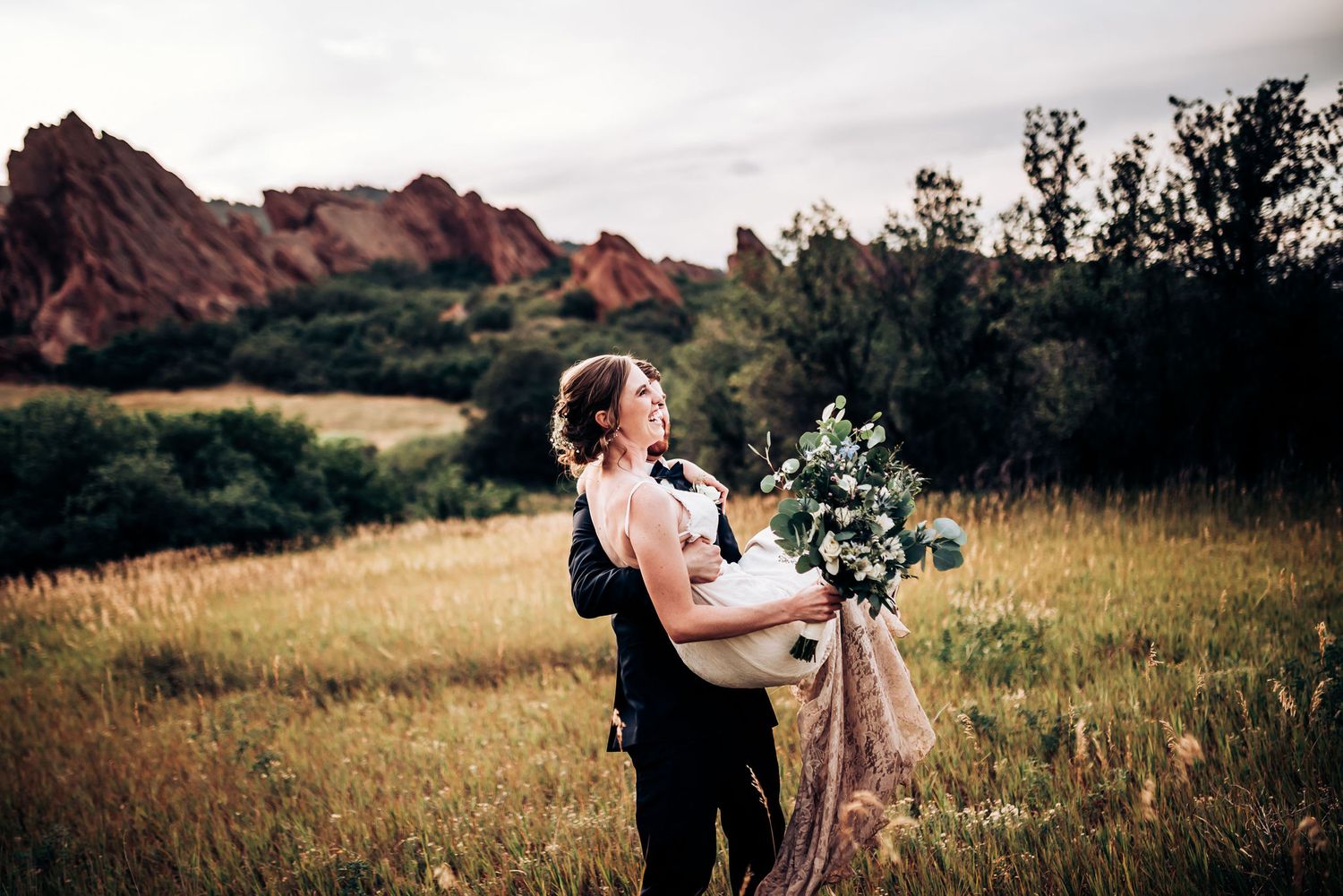 Wedding couple shares romantic moment with bouquet in mountain meadow.