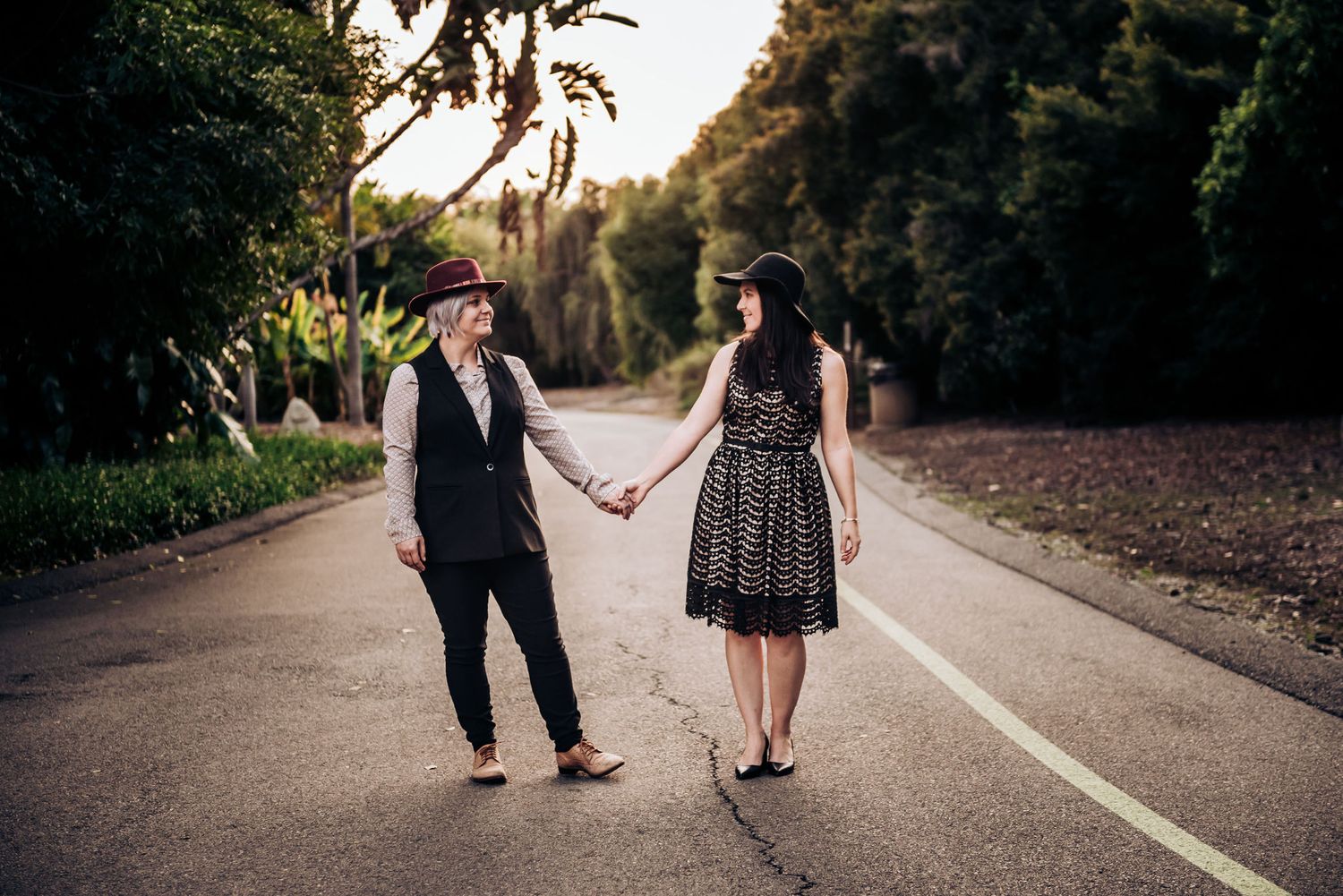 Two people walk hand in hand down a curved garden path surrounded by greenery.