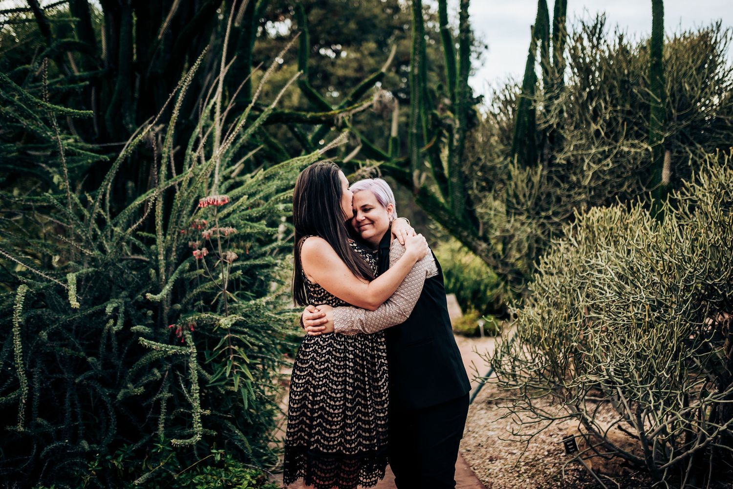 An affectionate embrace on a garden path surrounded by desert plants and cacti.
