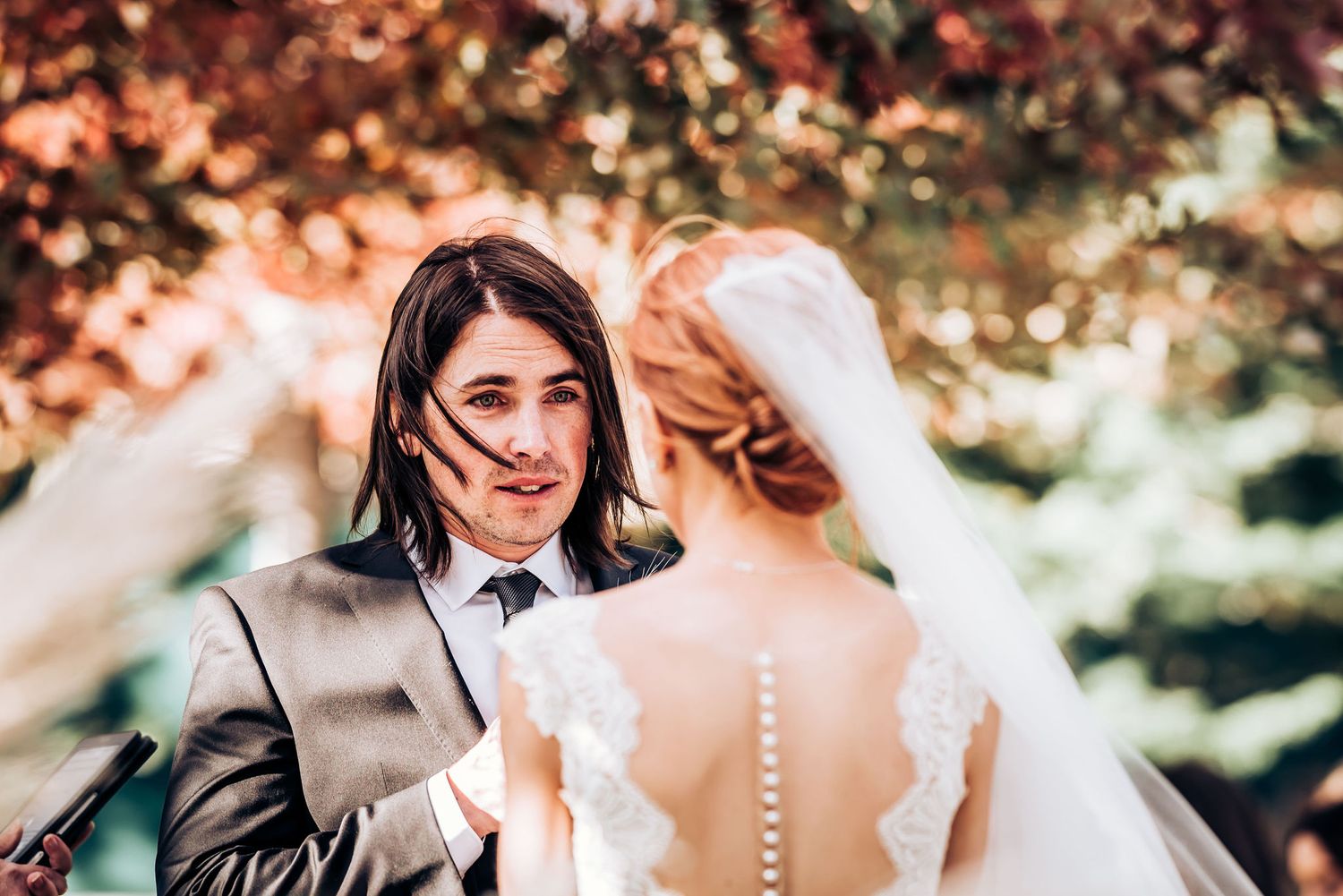A candid wedding ceremony moment captured outdoors with fall foliage in the background.