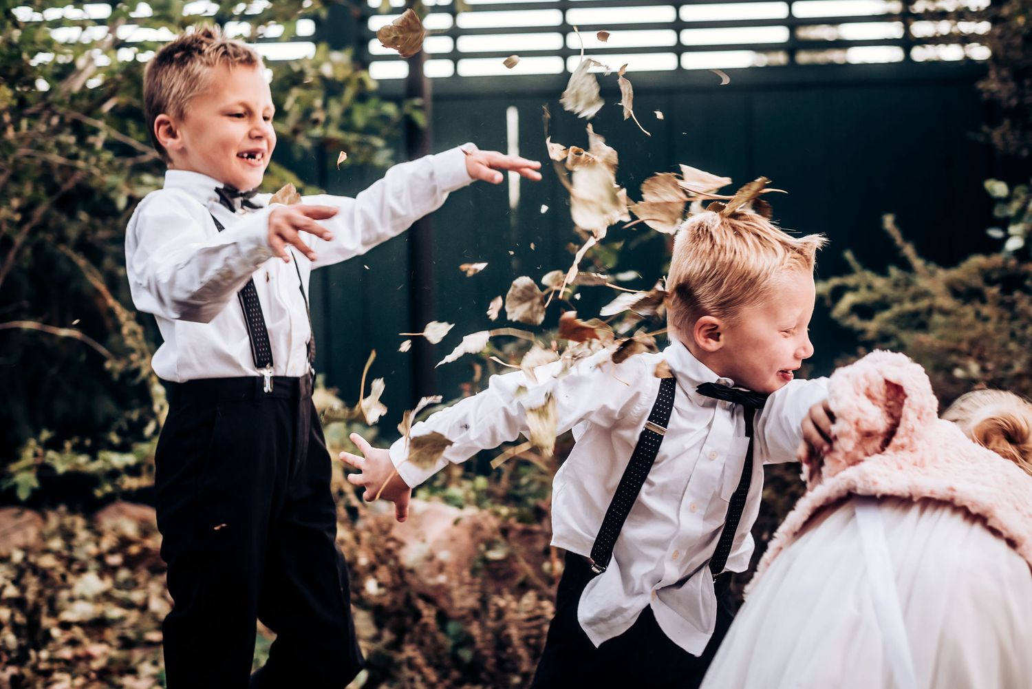Young children in formal attire playing with falling leaves at outdoor event.