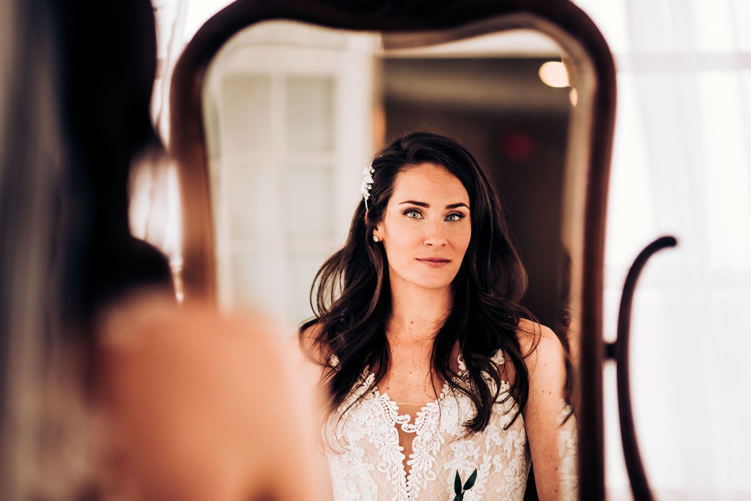 Bride looking at reflection while getting ready in elegant bridal gown.