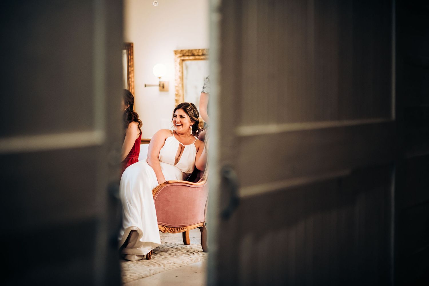 View through doorway of someone sitting in pink chair in elegant getting-ready room.