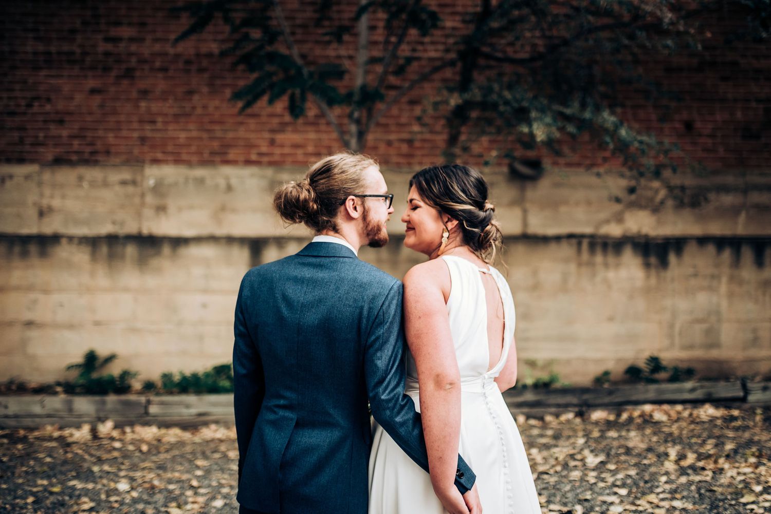 Romantic outdoor wedding portrait against rustic brick wall backdrop.