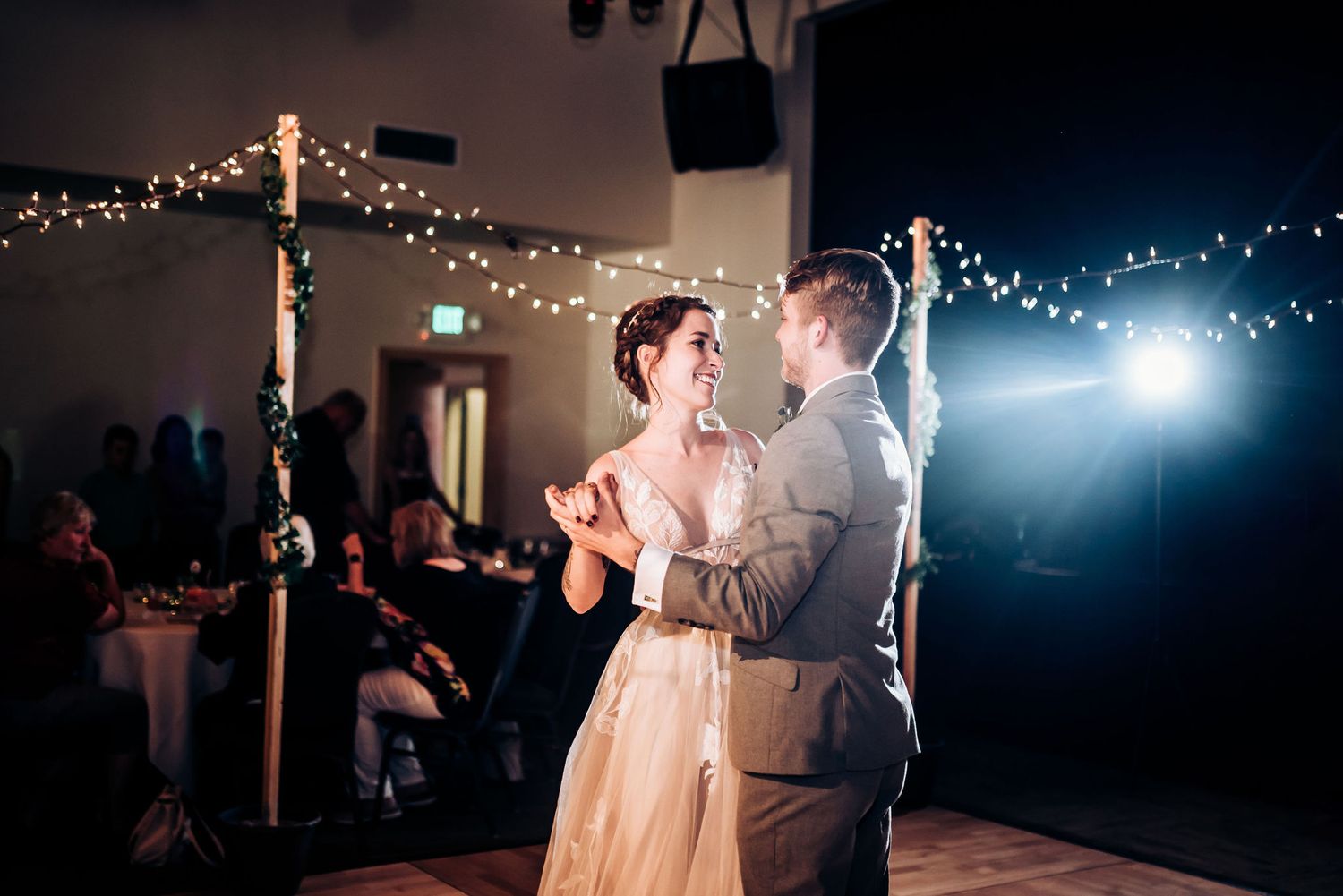 A romantic first dance illuminated by string lights and spotlights at an evening wedding reception.