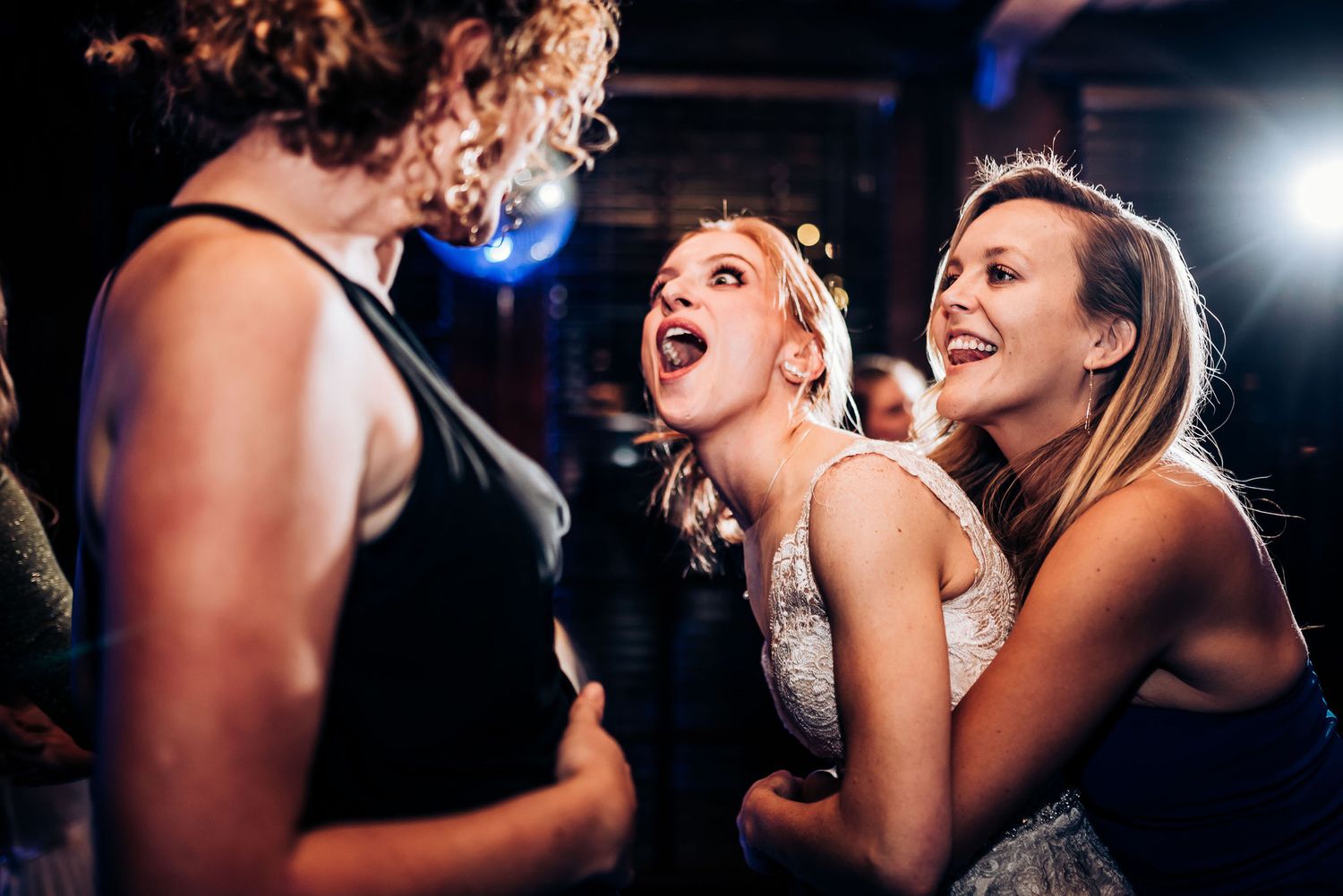 A group of friends sing and dance together at a party under bright spotlights.