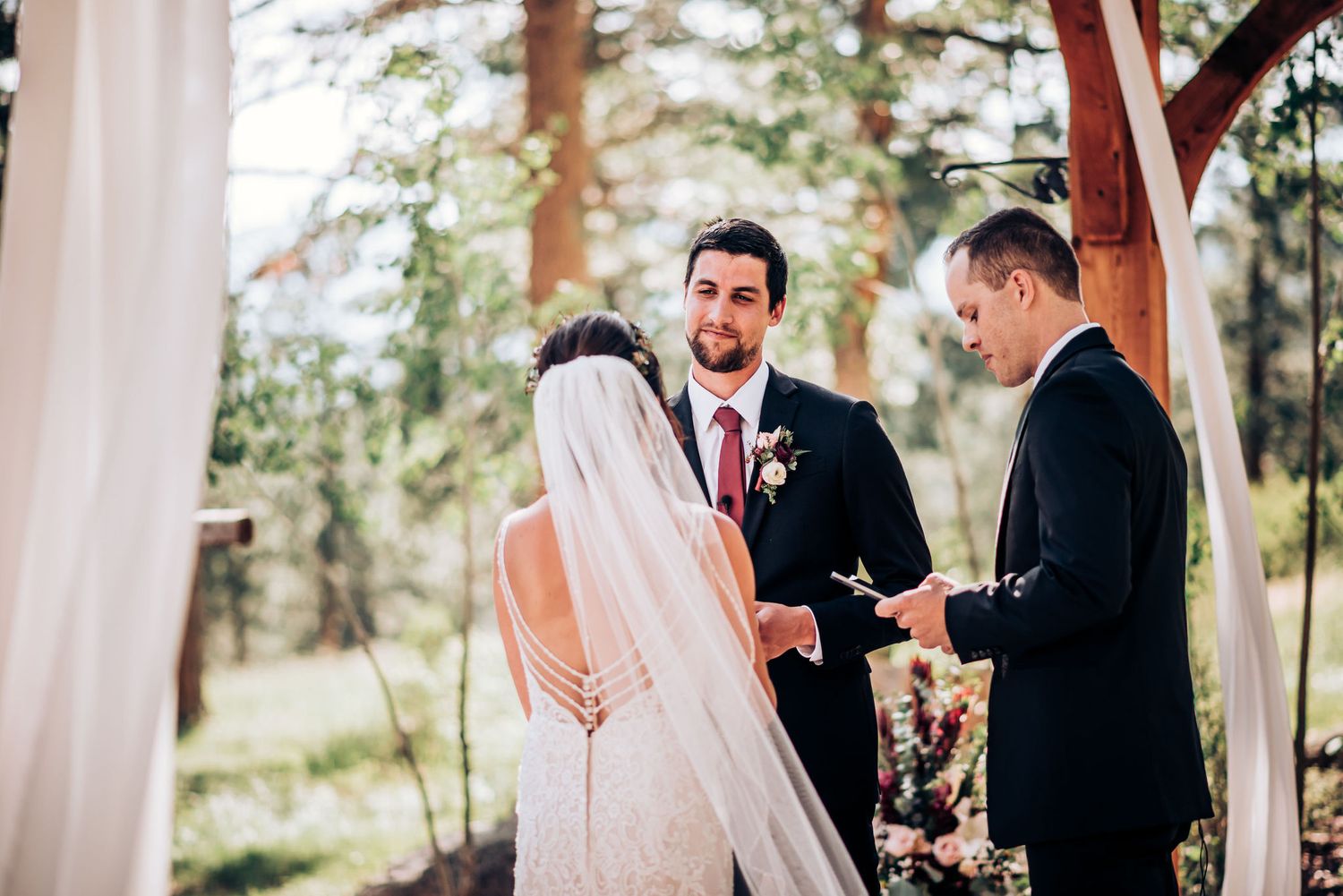 Intimate wedding ceremony moment under wooden pergola with flowing white drapes.