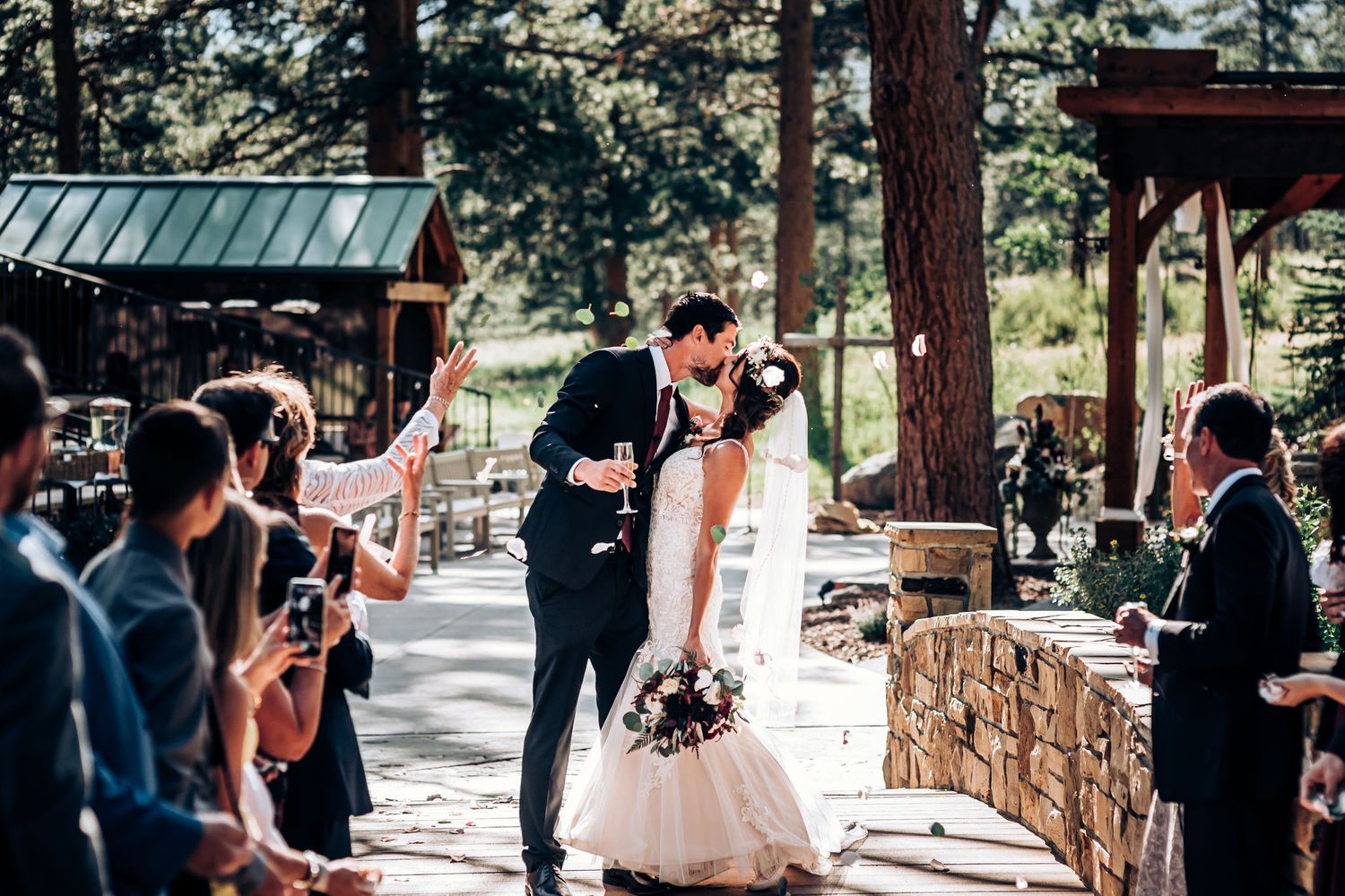 A couple shares their first kiss as guests applaud at an outdoor wedding venue.