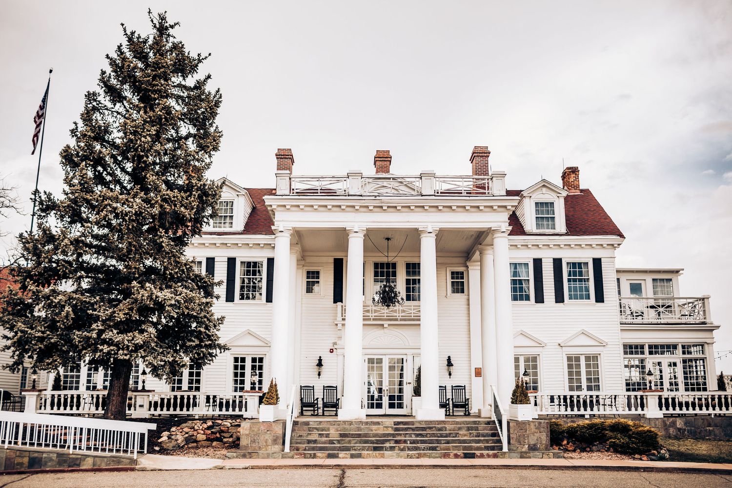 A grand white colonial mansion with black shutters and classical columns on its front porch.