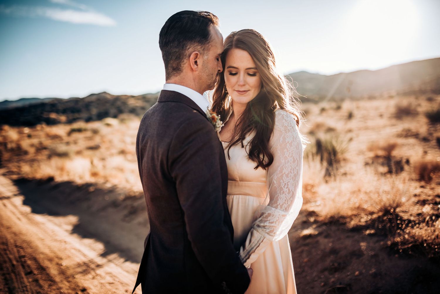 A couple shares an intimate moment in a desert setting during golden hour.