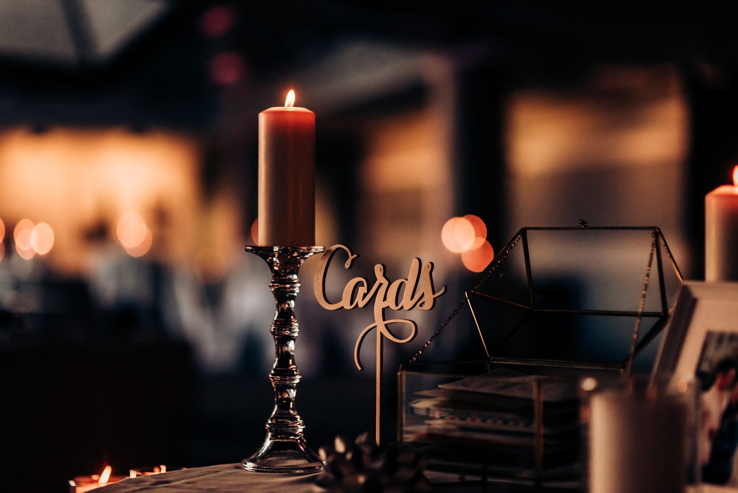 Elegant lit candle in ornate holder with decorative 'Cards' sign at wedding reception in romantic lighting.