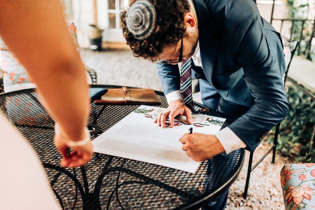 Someone signs documents on an outdoor patio table during a wedding event.