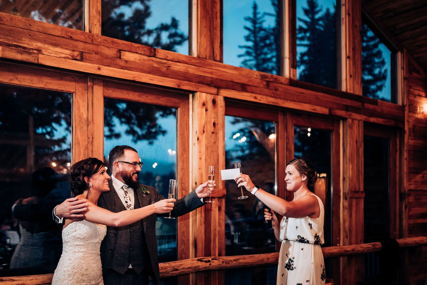 Wedding party toasts together at rustic wooden lodge during evening celebration.