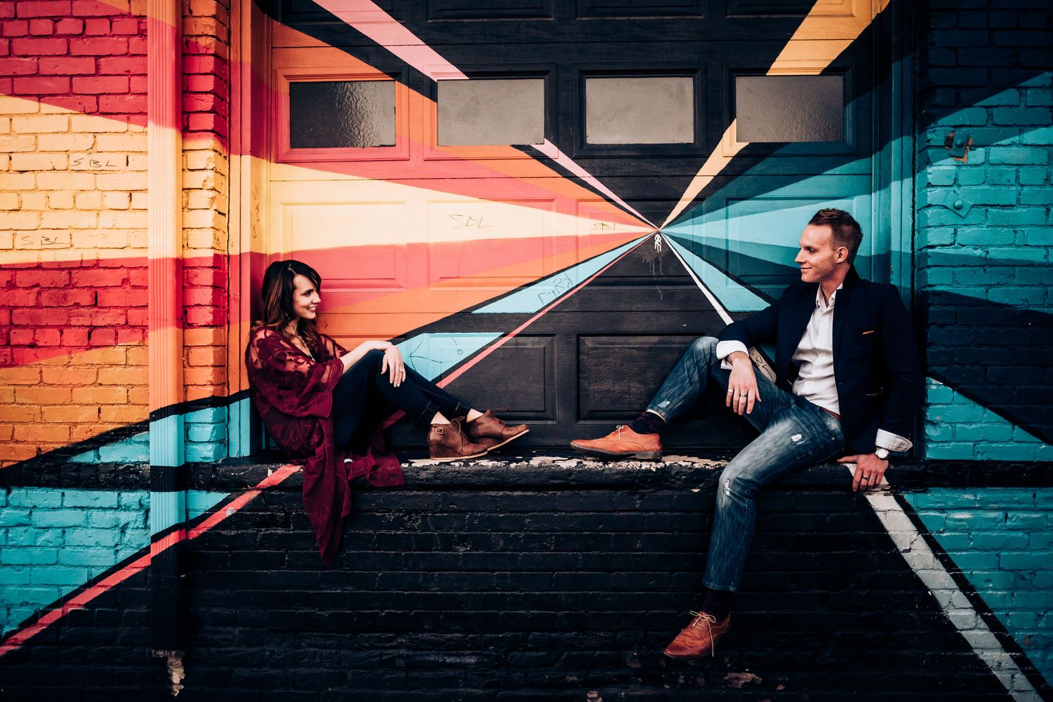Couple relaxes on steps in an urban tunnel with vibrant geometric wall designs.