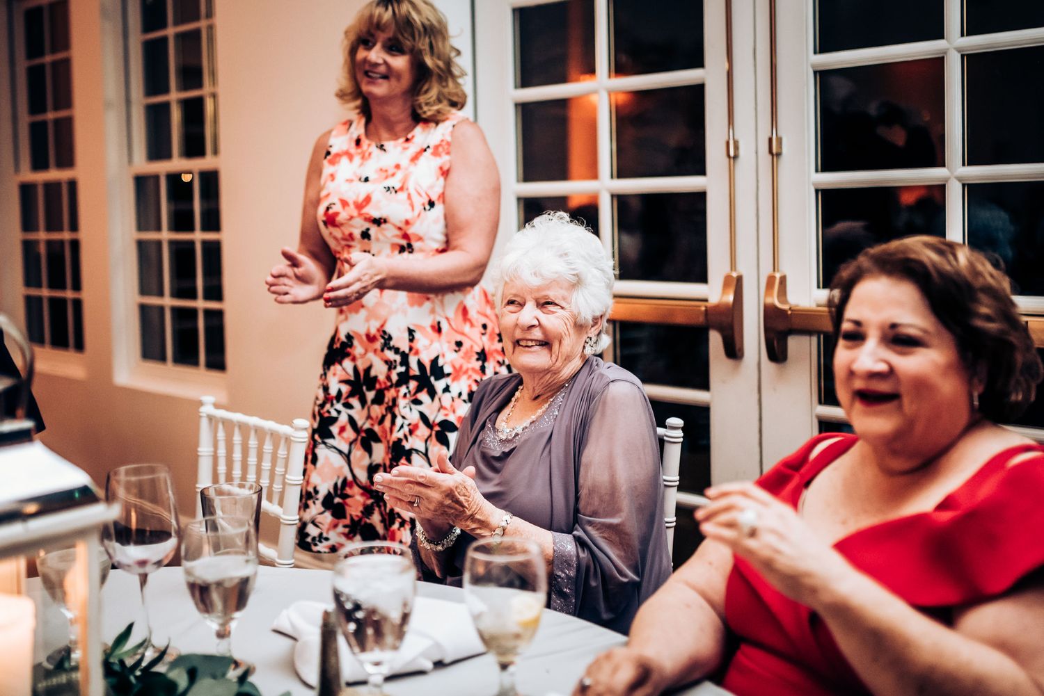 Wedding guests in colorful attire laugh and enjoy themselves at reception tables.