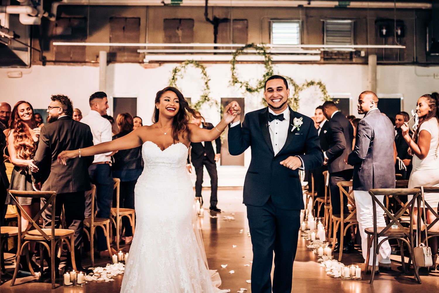 Joyful couple celebrates while walking down aisle at modern indoor wedding venue.