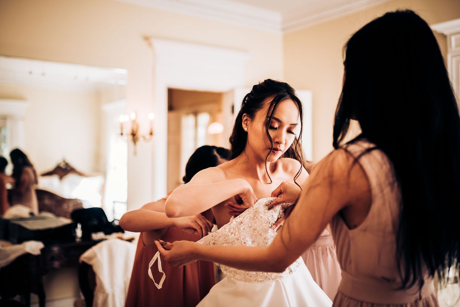 Wedding preparations showing a dress being adjusted in an elegant room with warm lighting.