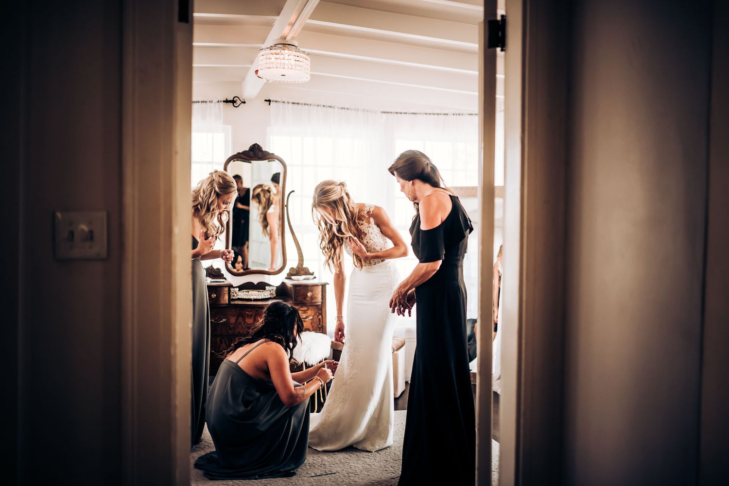 Behind-the-scenes view of wedding dress preparation with helpers in dark attire.