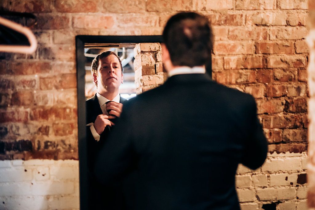 A reflection in a mirror shows someone adjusting their outfit against a brick wall background.