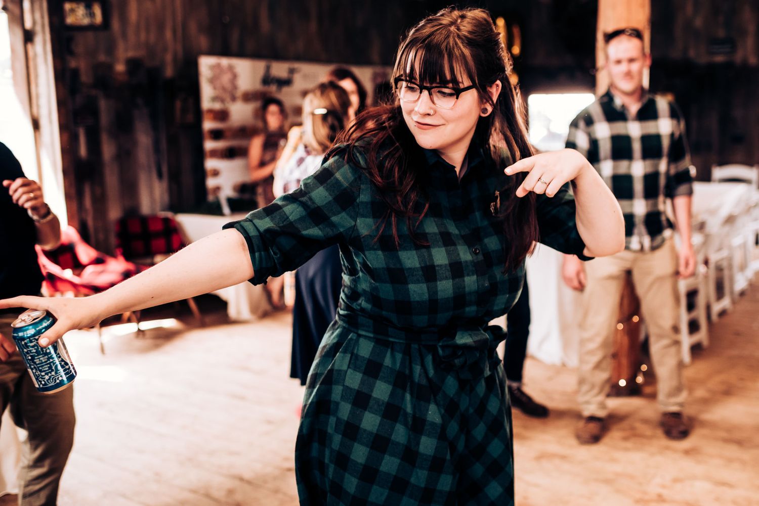 Person in buffalo check dress dances enthusiastically at rustic barn celebration.