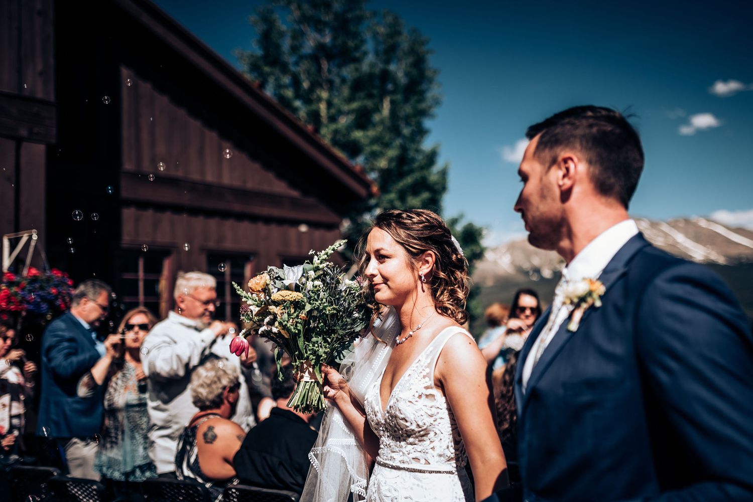 Outdoor wedding celebration at rustic mountain venue with pine trees in background.