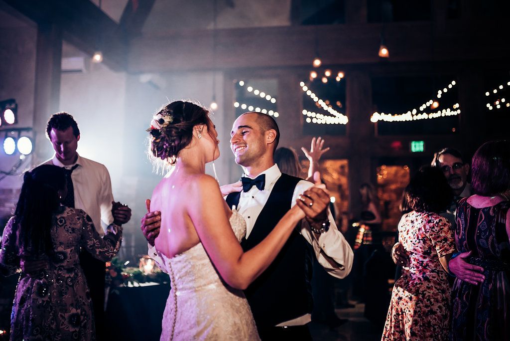 A romantic first dance between newlyweds at their wedding reception with twinkling lights in the background.
