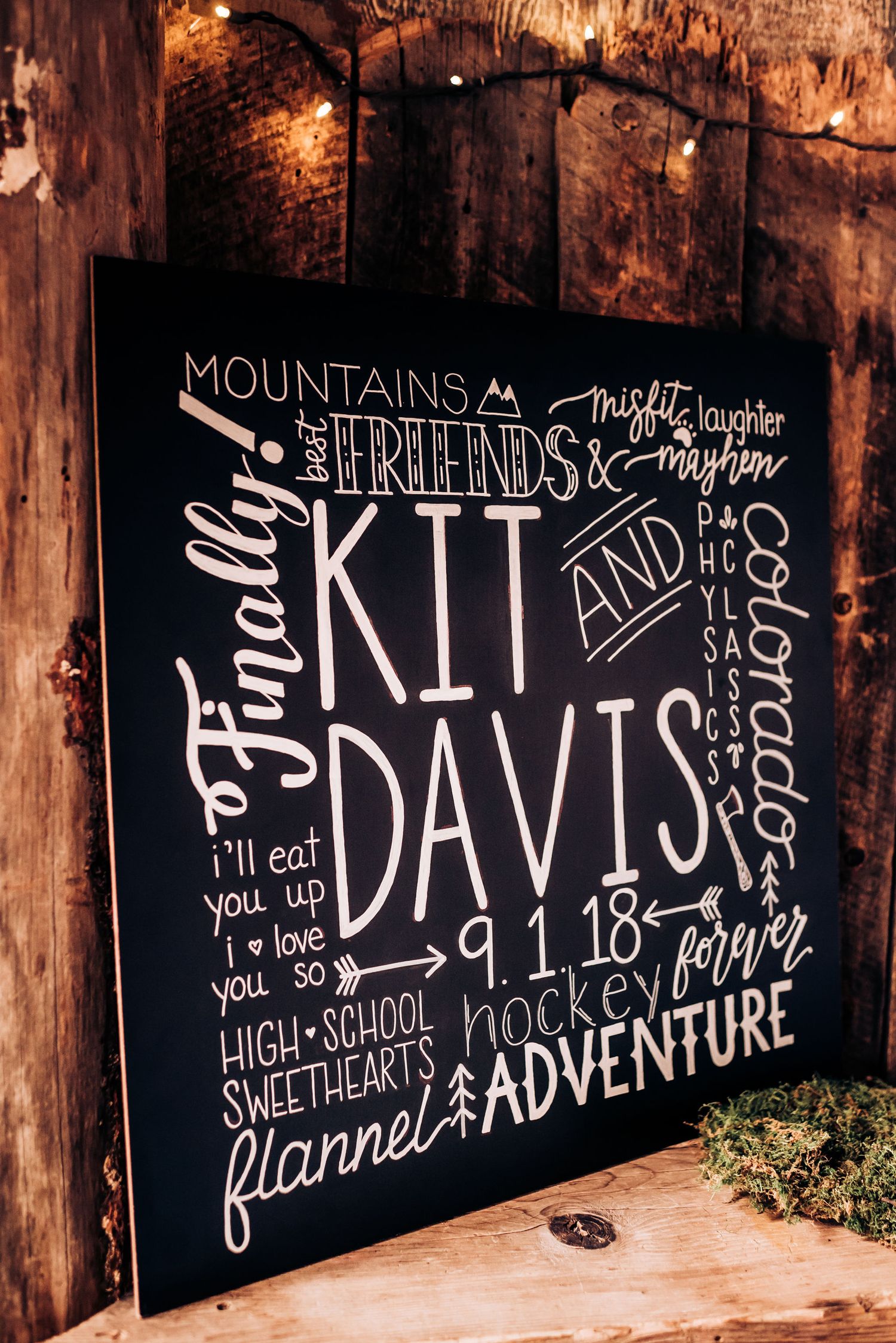 Black chalkboard wedding sign with hand-lettered text featuring mountains and adventure themes.