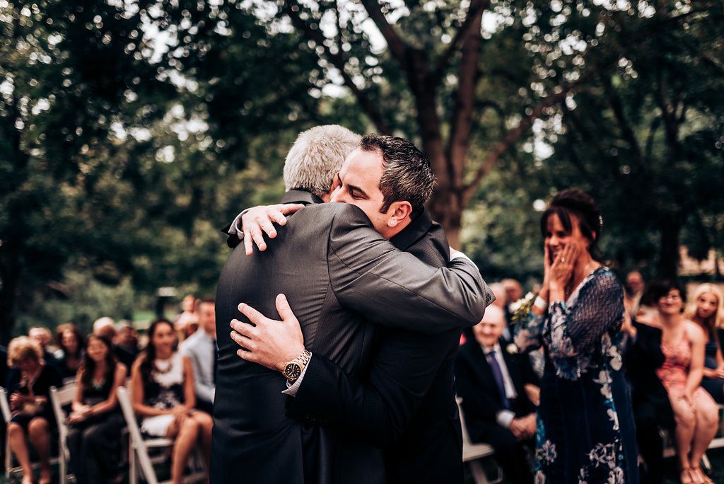 Emotional embrace during outdoor wedding ceremony with guests watching.