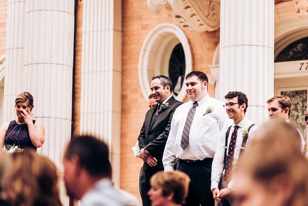Guests gather on ornate steps with classic columns during an outdoor wedding ceremony.