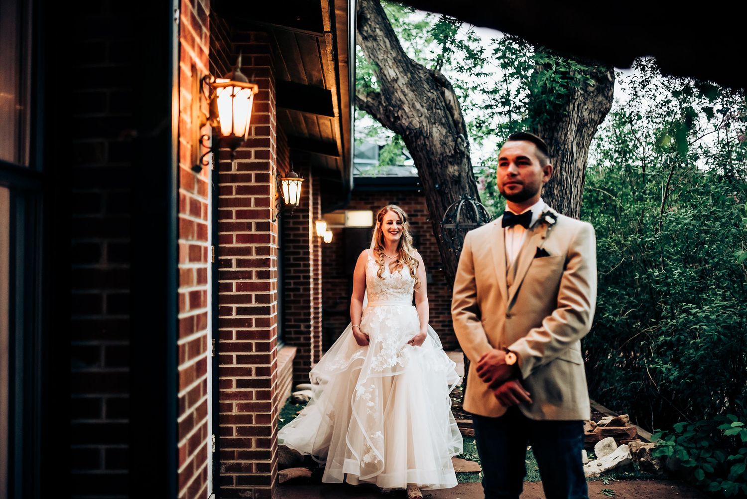 A wedding moment captured outside a brick building with warm lantern lighting at dusk.