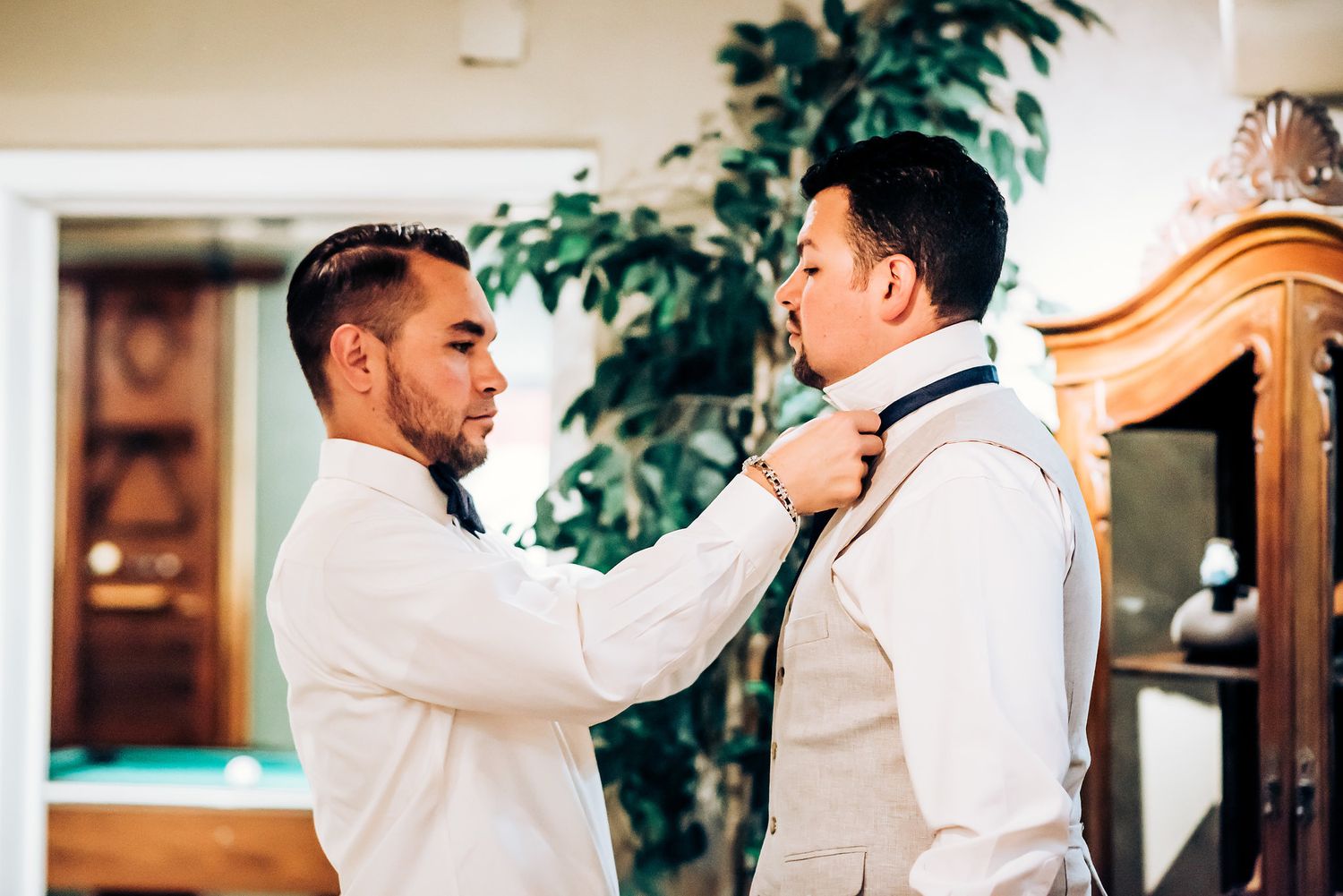 Two people in white adjusting formal attire before a wedding ceremony.
