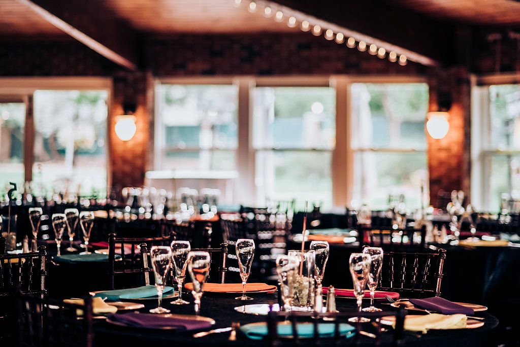 Empty wedding reception tables set with dark chairs and romantic lighting.