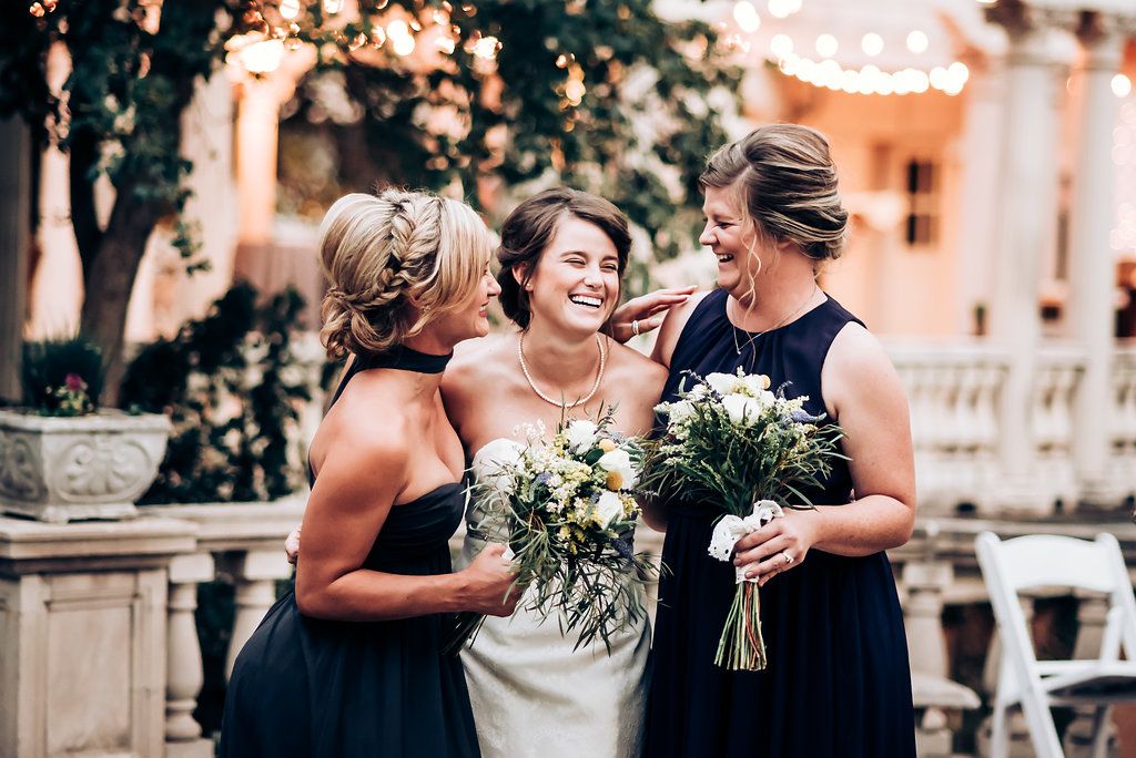Wedding party members sharing a joyful moment outdoors while holding bouquets.