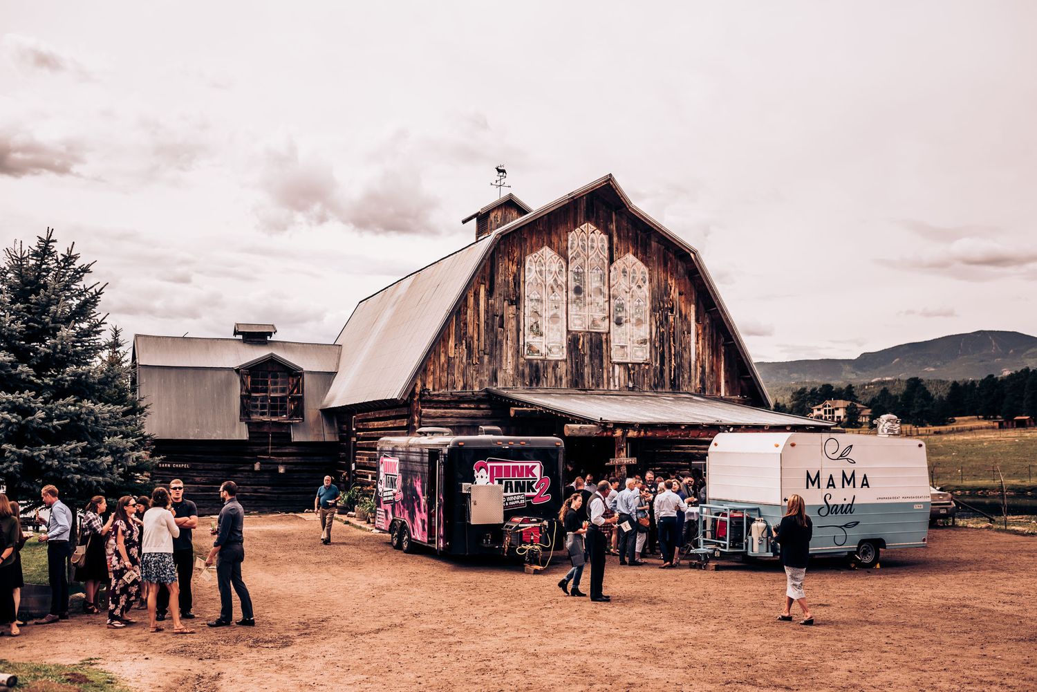 Rustic barn venue with food trucks and gathering crowd during an outdoor event.