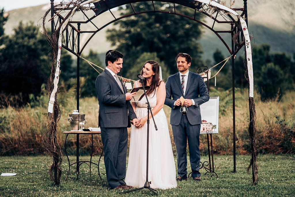 Wedding ceremony under rustic wooden arch with ceremony taking place at mountain venue.