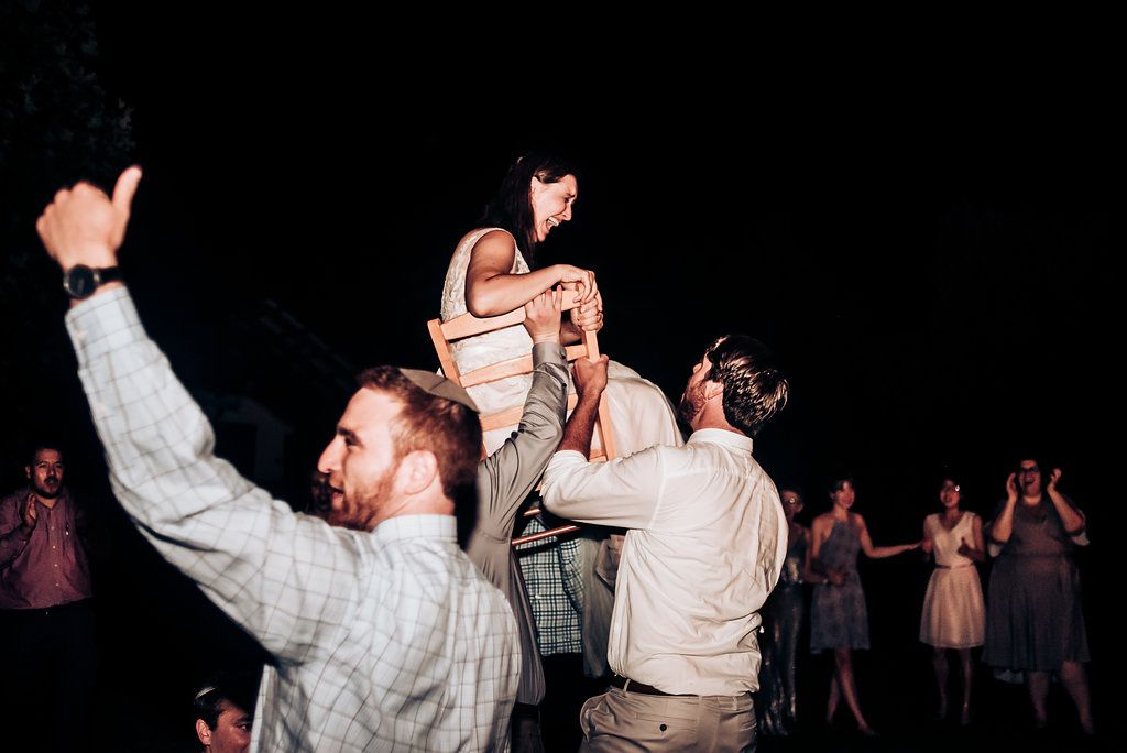 Celebratory moment with guests lifting someone during nighttime wedding festivities.