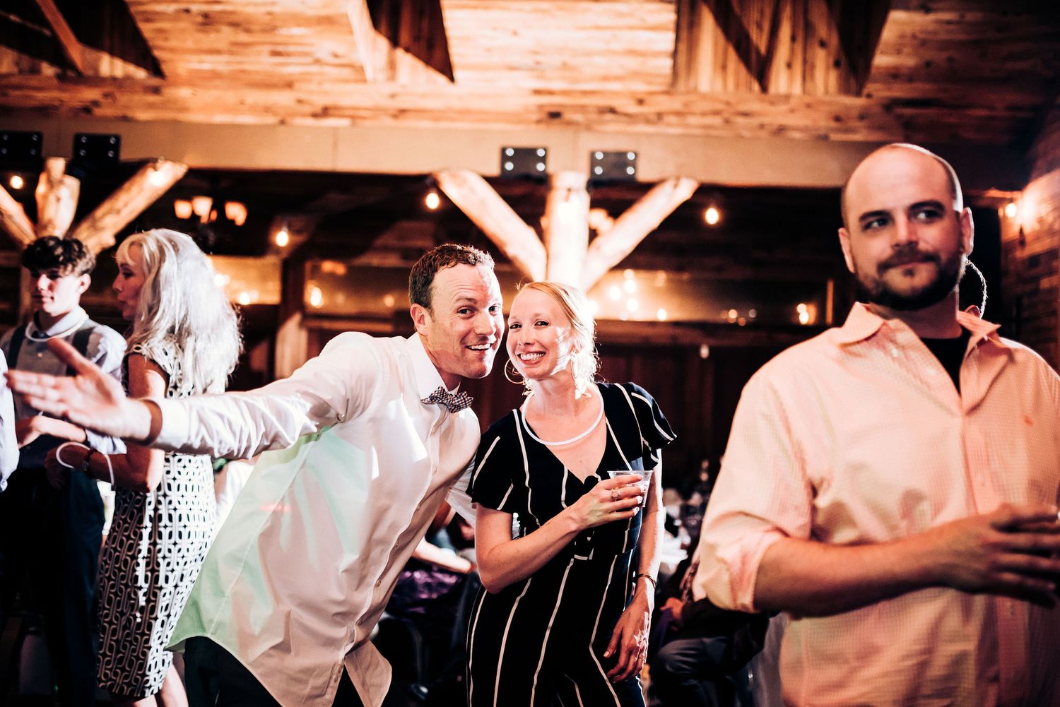 Wedding guests dancing and celebrating at rustic indoor venue with wooden beams.
